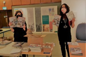 Two women wearing face masks holding up booklets