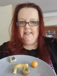 Photograph of a woman holding a plate of small fruits made from marzipan