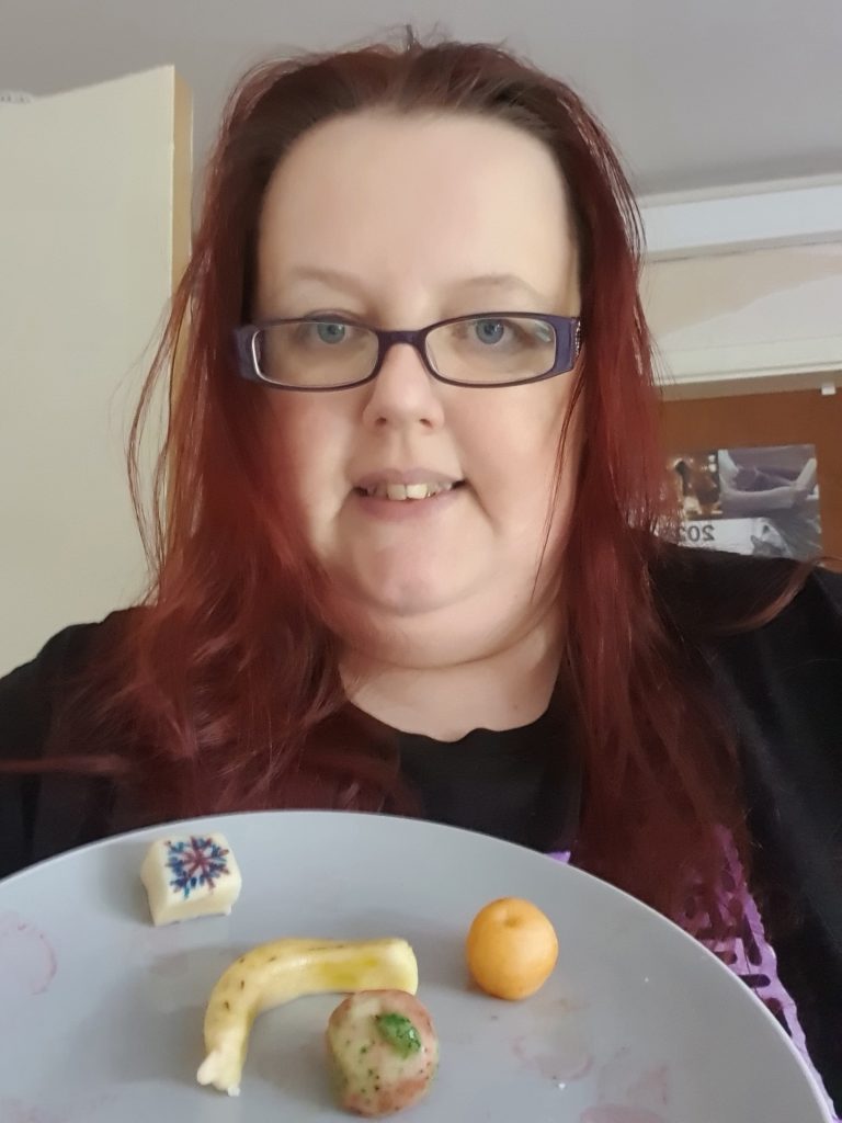 Photograph of a woman holding a plate of small fruits made from marzipan