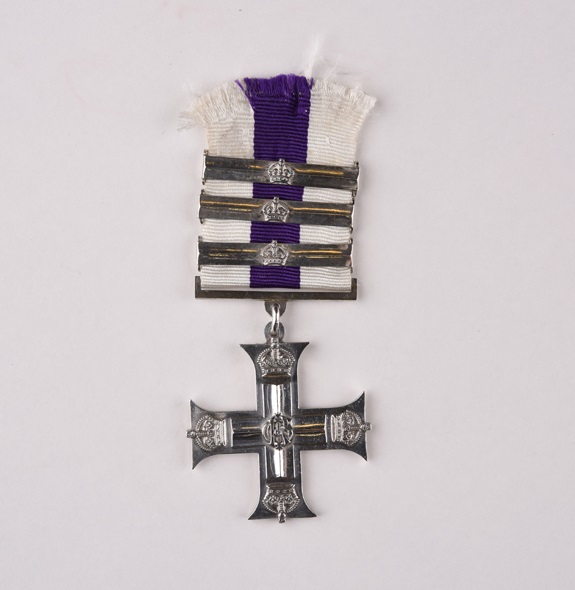 A cross shaped ribbon with a purple and white striped ribbon, three metal bars across the ribbon