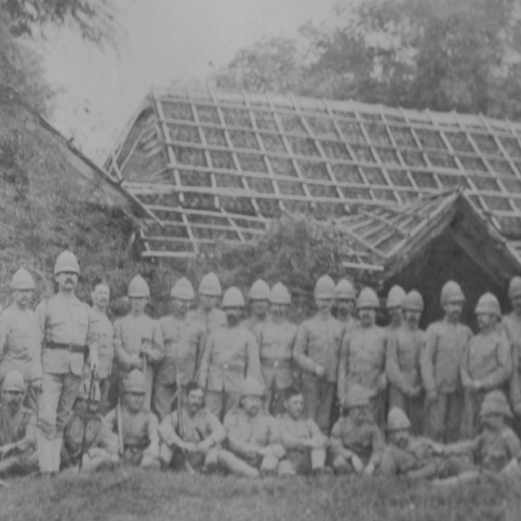 black and white photograph of soldiers wearing tropical uniforms in front of a wooden building