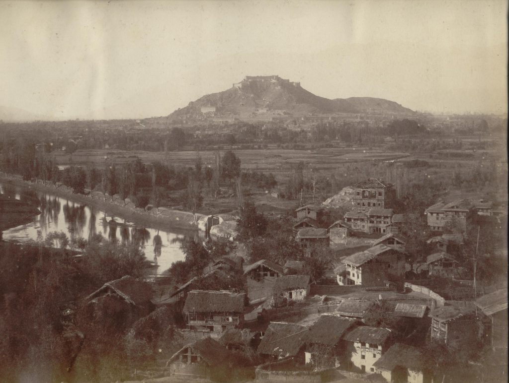 sepia photograph of buildings, river and mountainous landscape