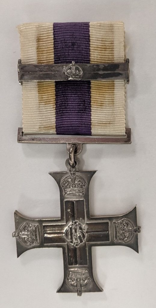Silver cross shaped medal with a white and purple striped ribbon and a metal bar across the ribbon